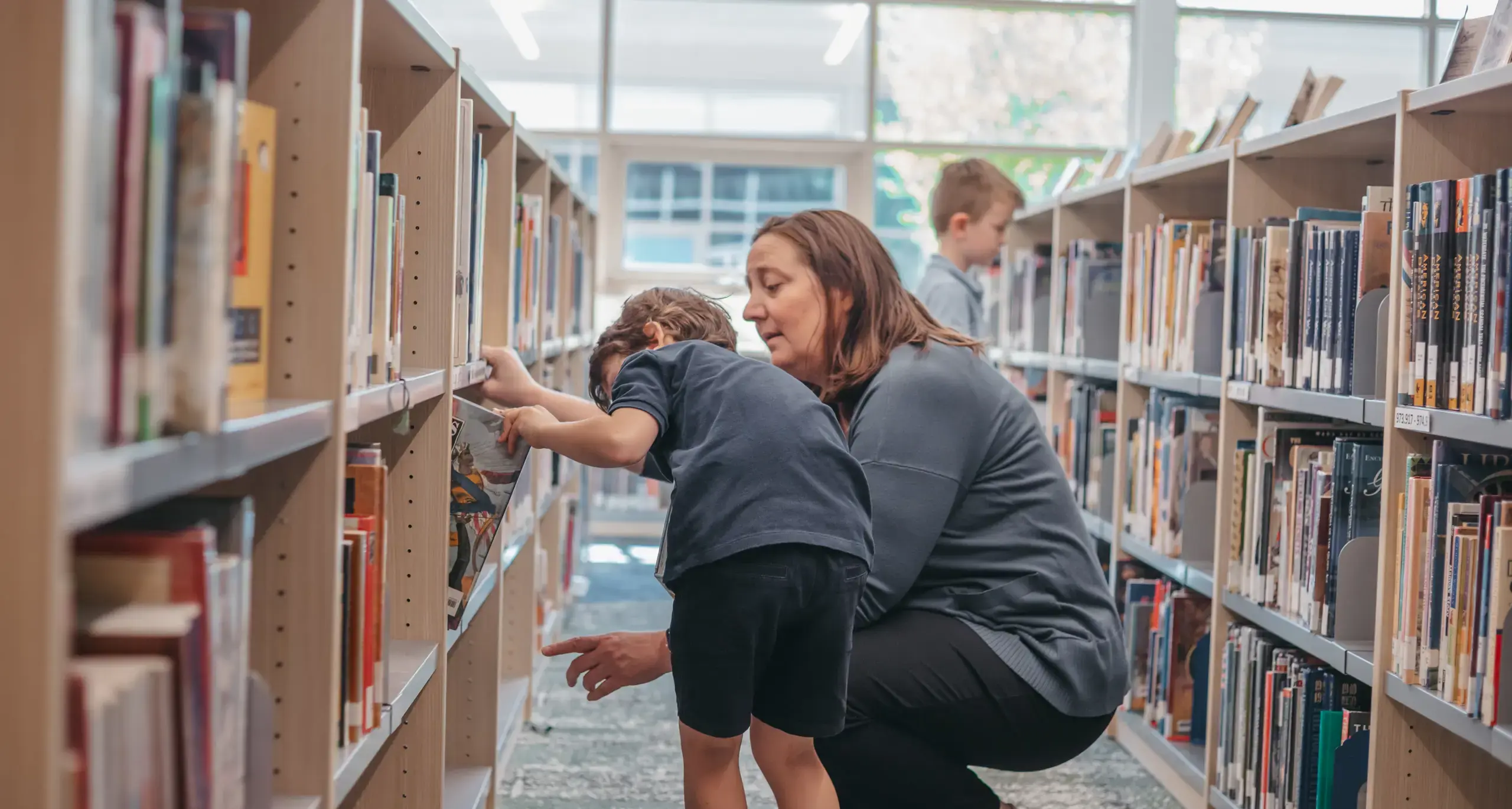 Teacher helping a young student find books in the library.