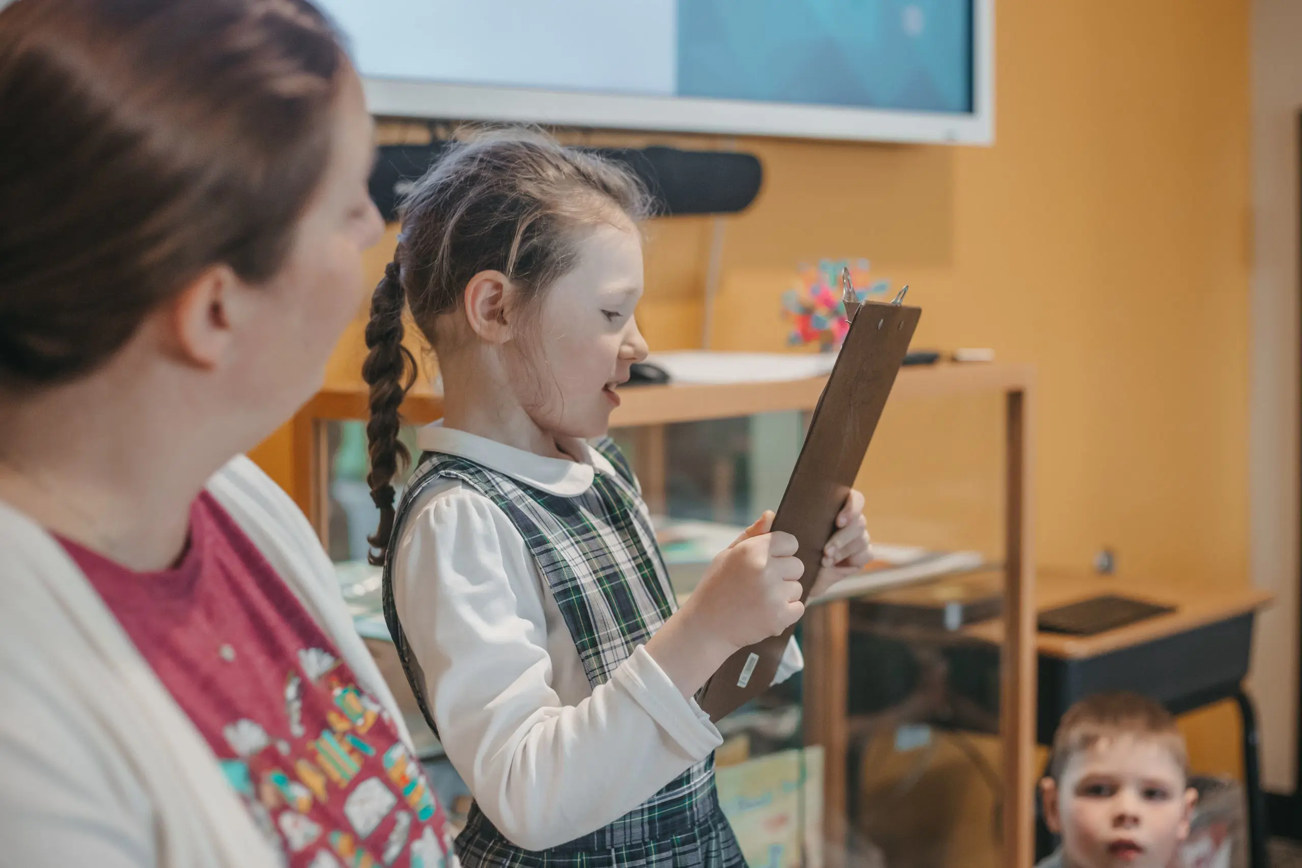 Young student presenting to classmates with a clipboard.