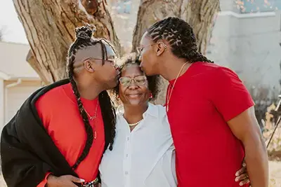 Two alumni kissing their mom on the forehead outdoors