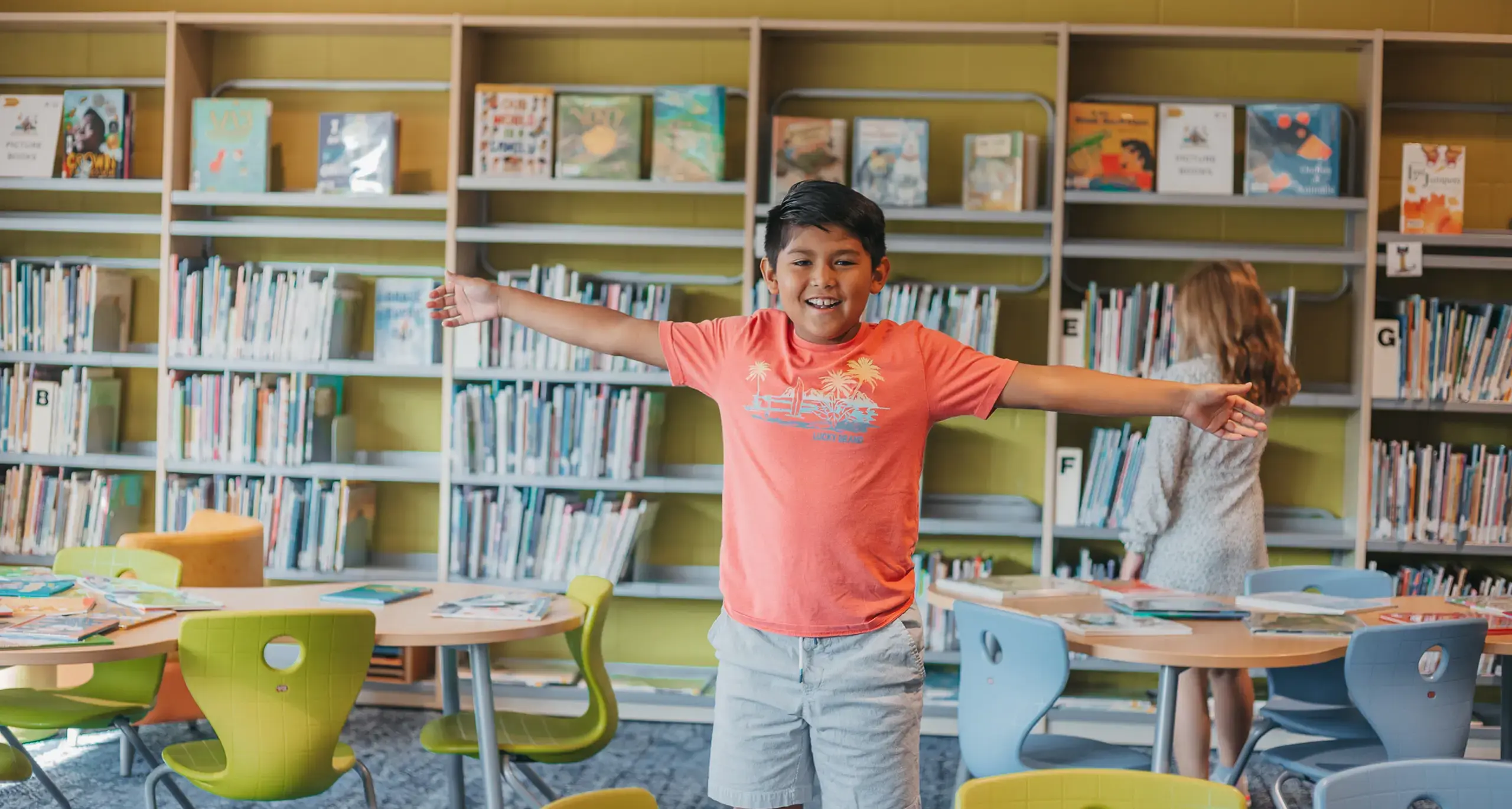 Student smiling with arms outstretched in the school library