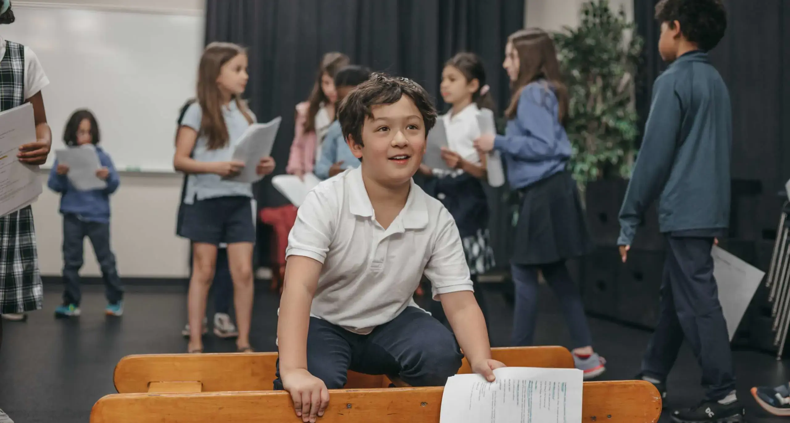 Student rehearsing with classmates on a school stage.