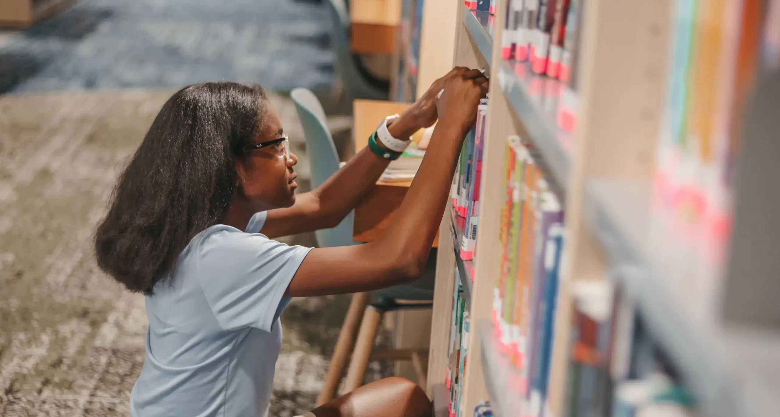 Student selecting books from the school library shelves