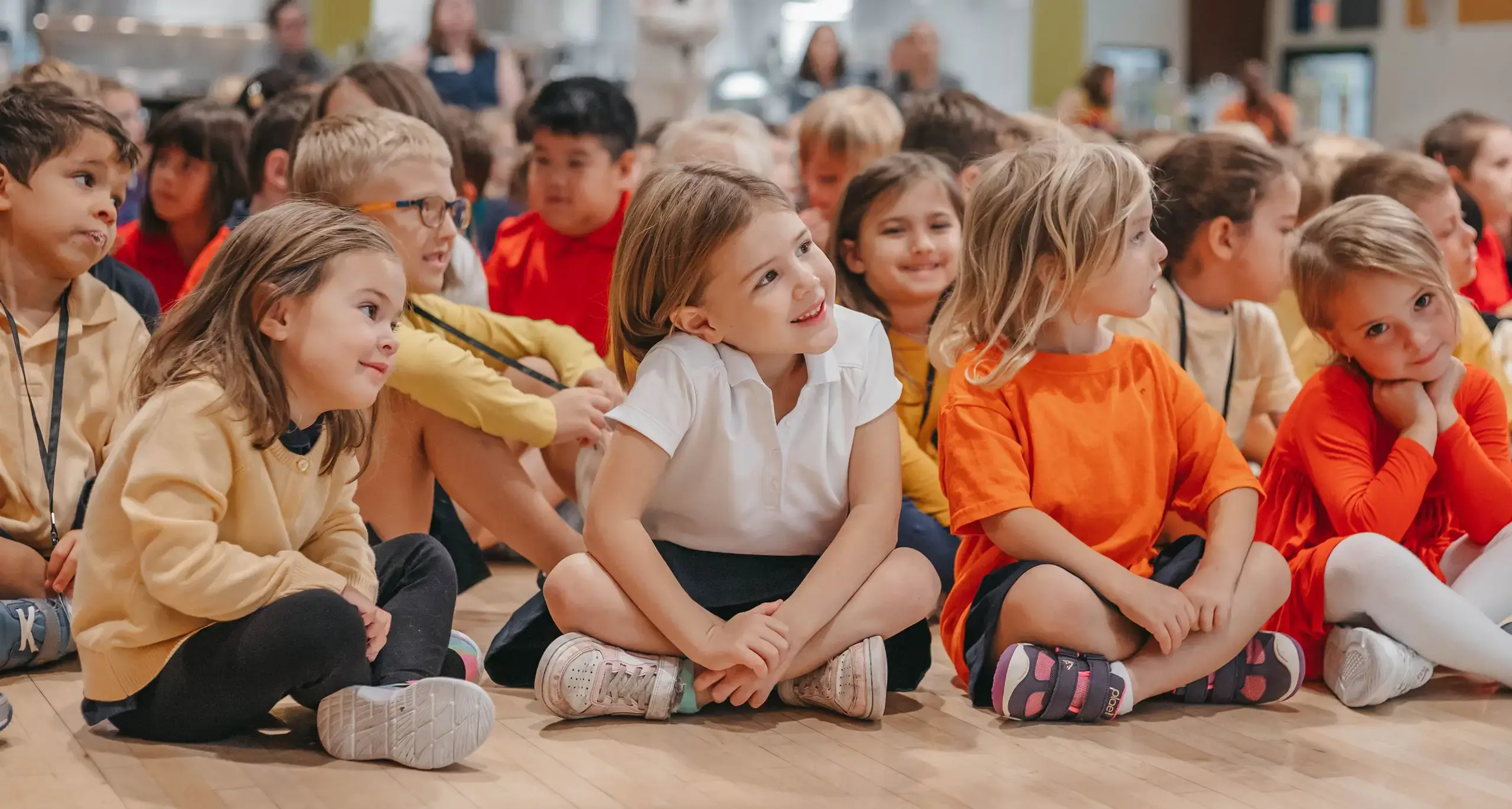Lower school students sitting on the floor, smiling and engaging with their teacher