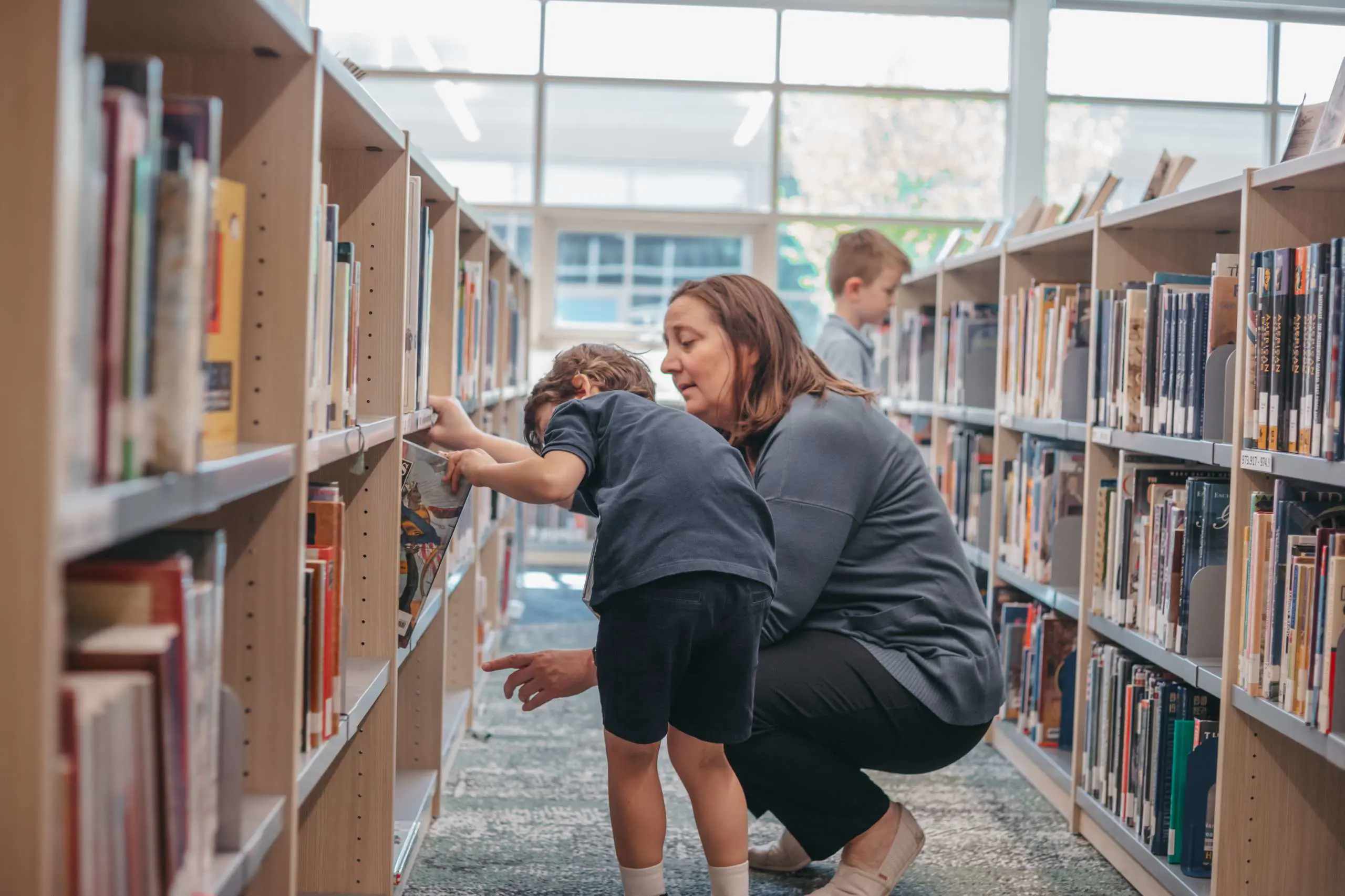 Teacher helping student to choose a book from the library
