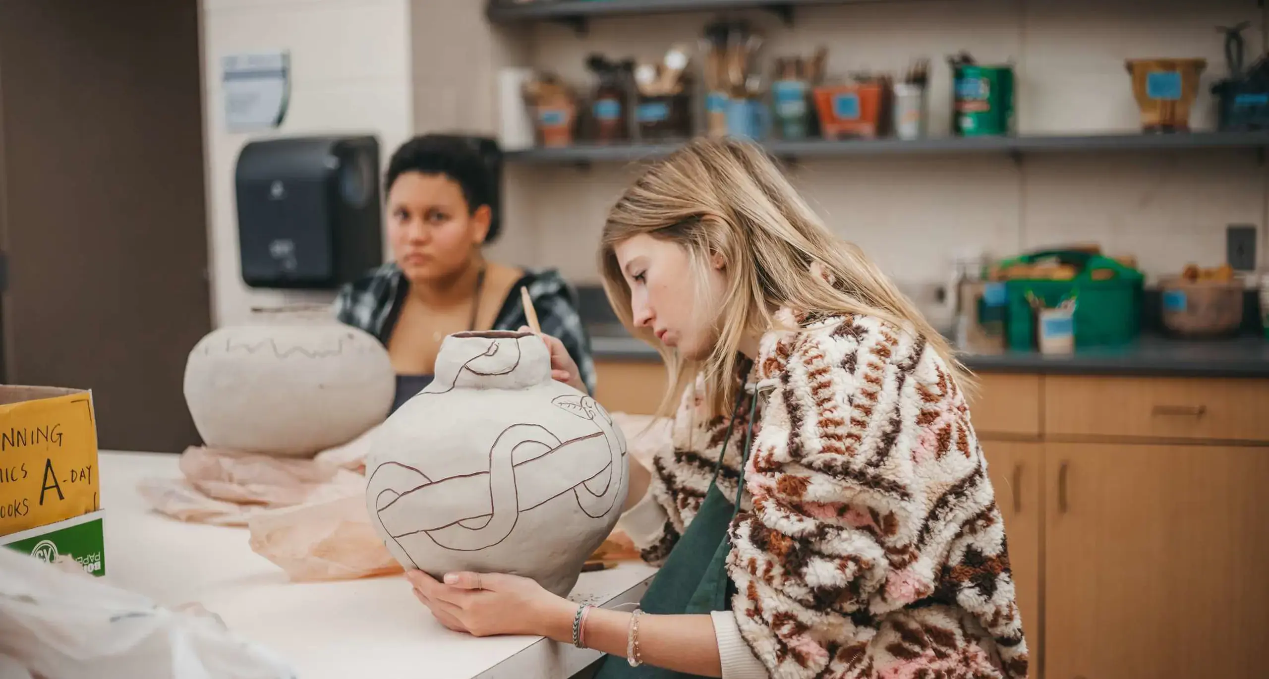 Student painting a ceramic vase in art class.