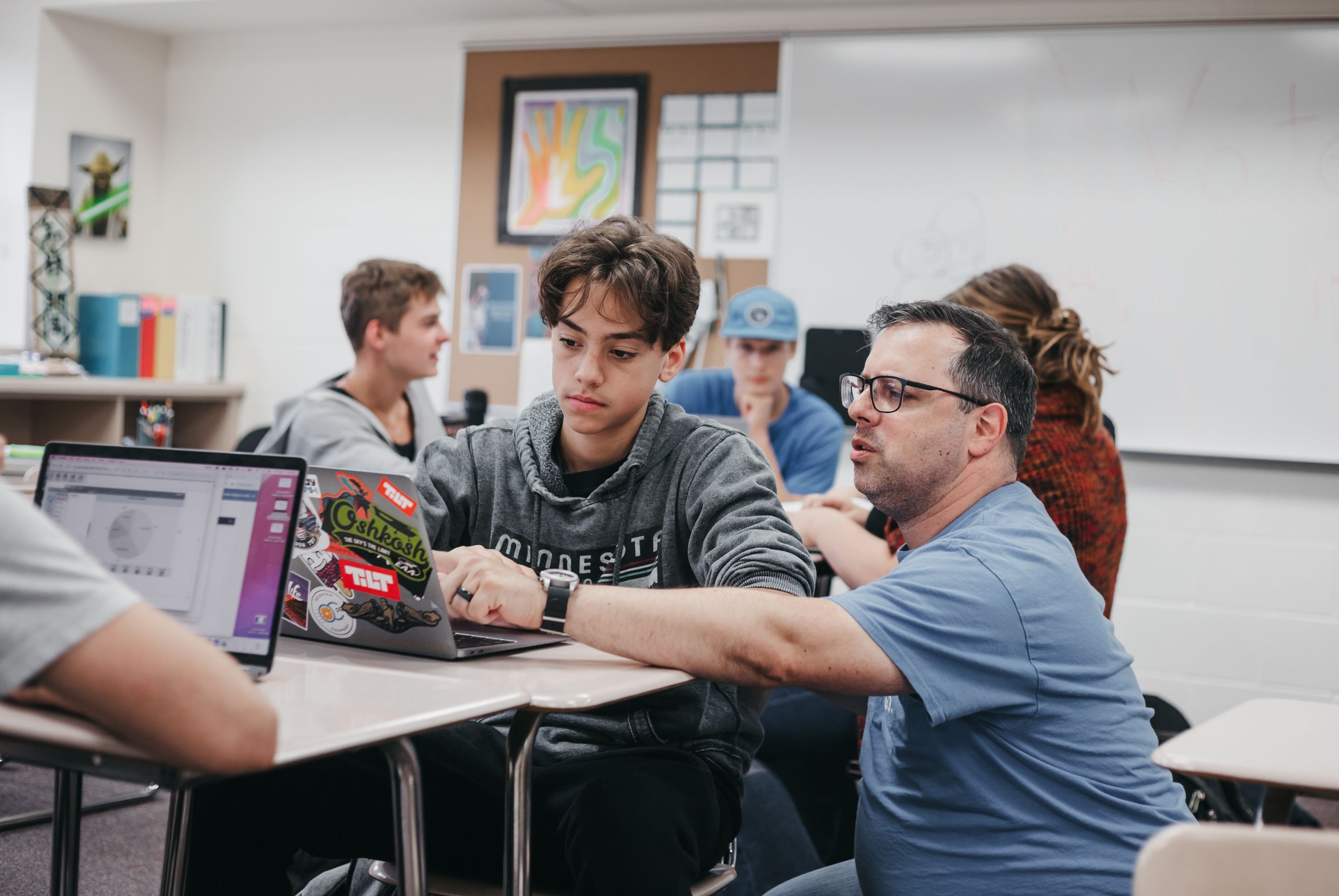 Teacher guiding a student during a classroom lesson.