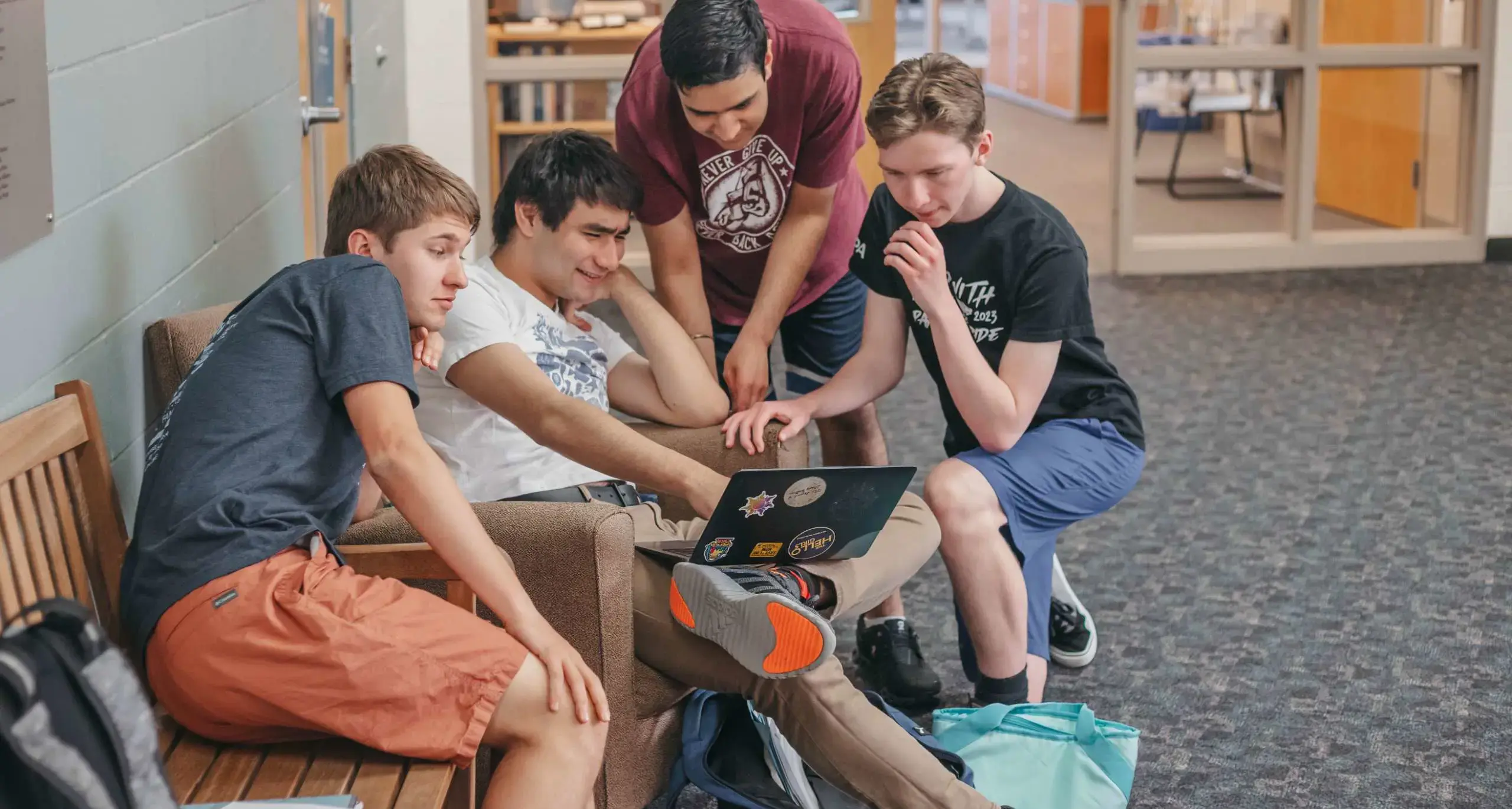 High school students collaborating around a laptop in a common area.