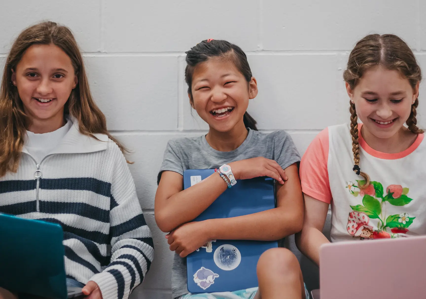 Three students smiling together while using laptops.