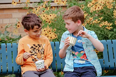 Two boys on a bench eating ice cream. 