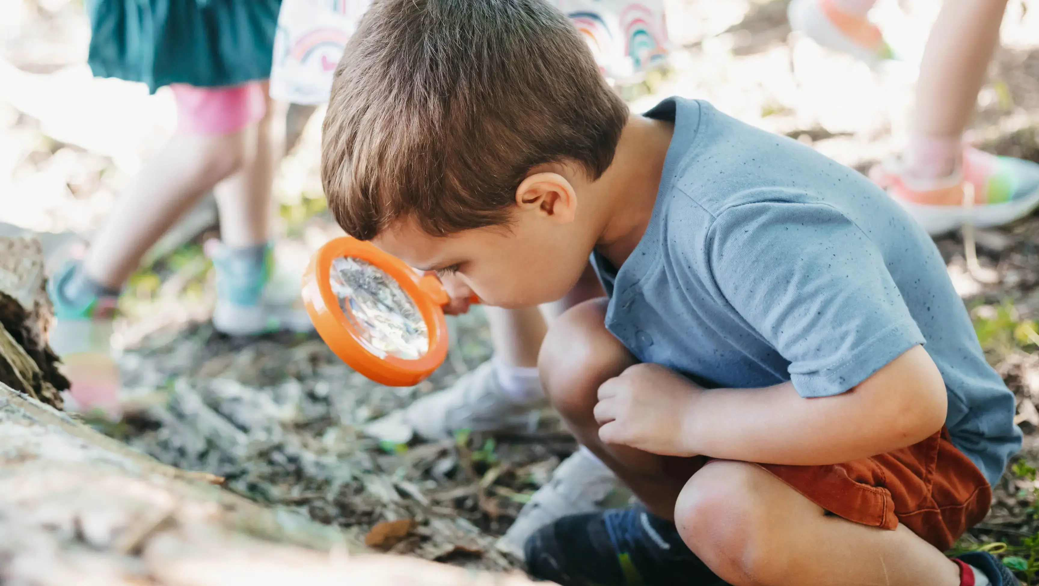 lower school student looking through a magnifying glass outdoors