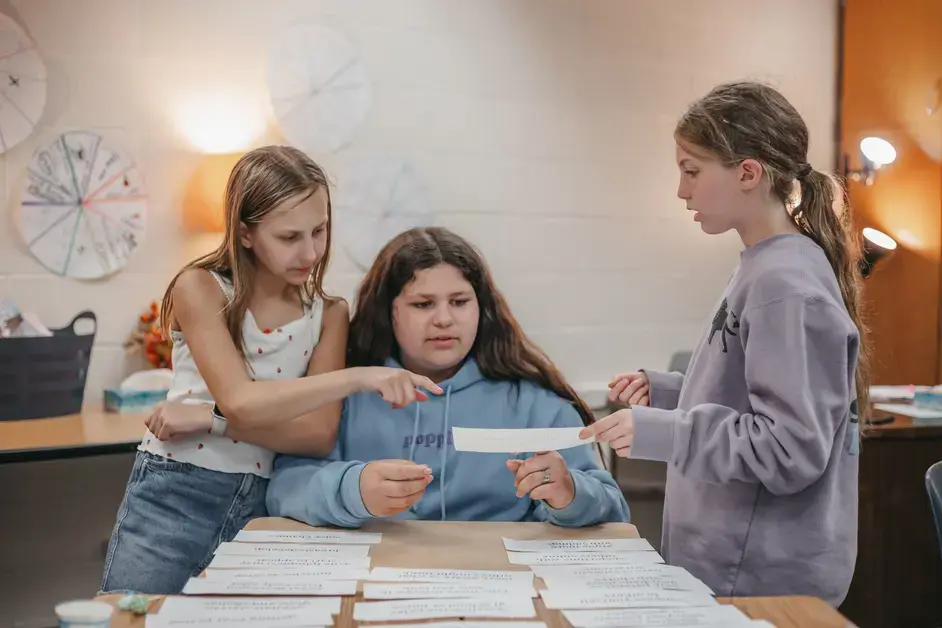 Three students collaborate on a classroom activity, reviewing and sorting information cards.