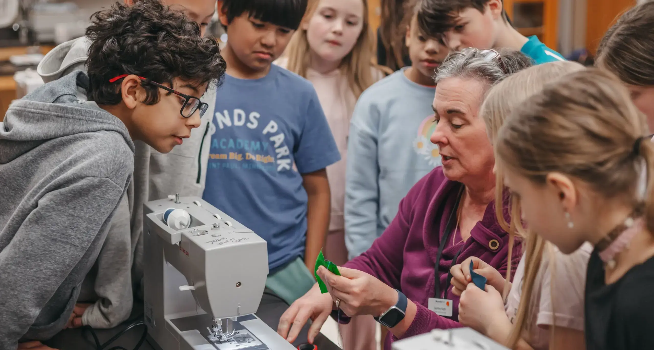 Teacher demonstrating sewing techniques to middle school students.