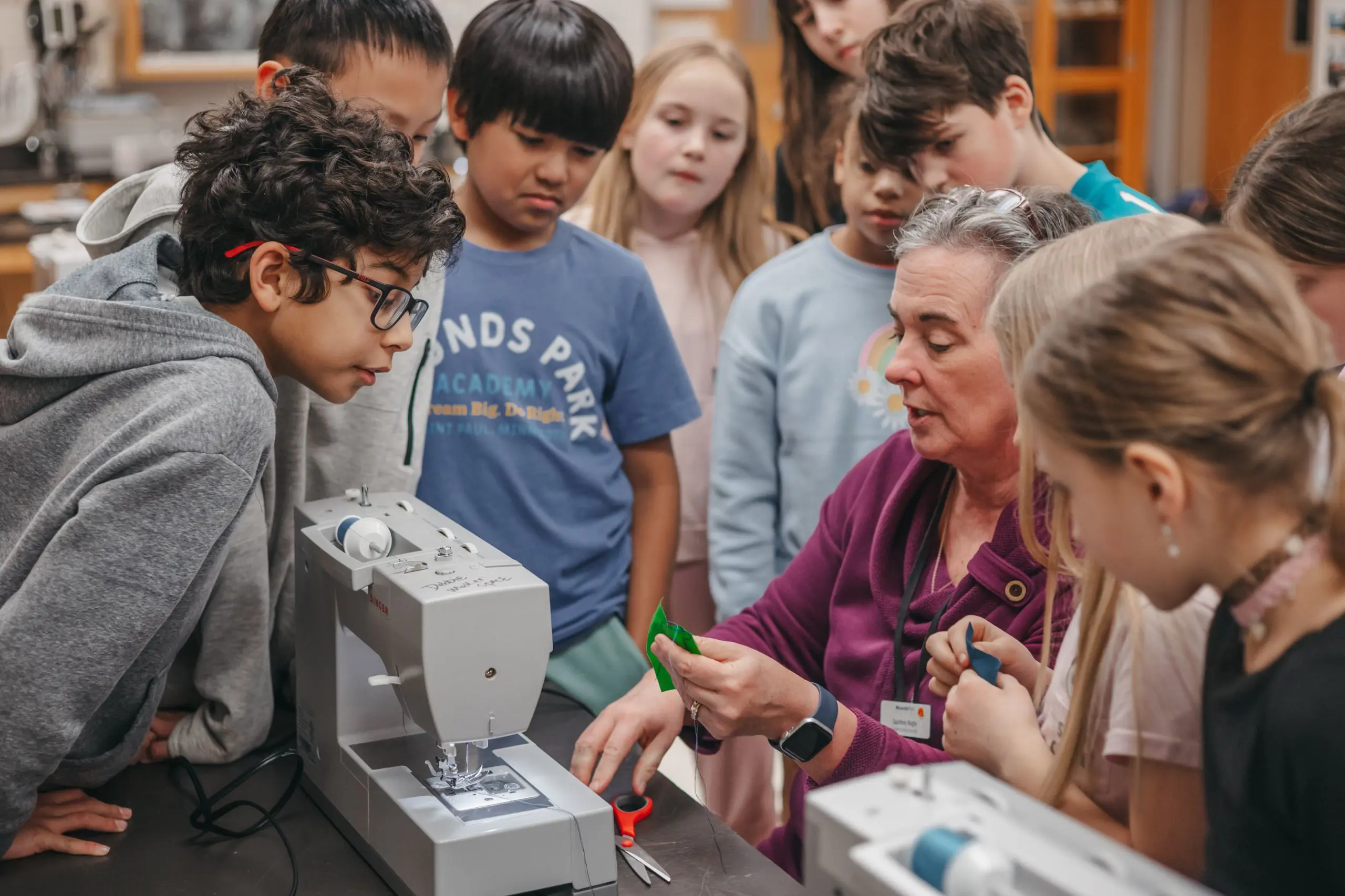 Teacher demonstrating sewing techniques to middle school students.